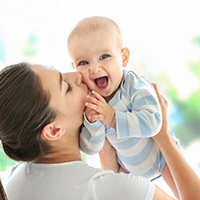 A young woman holding up her baby and kissing it on the cheek as it smiles