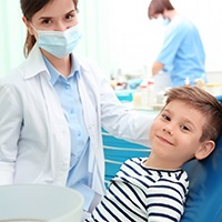 A little boy smiling in the dentist’s chair as the dental professional prepares to place dental sealants