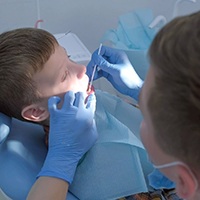 A dentist applying fluoride to a young boy’s smile during his checkup and cleaning appointment