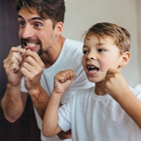 A father and son flossing their teeth in the mirror at home