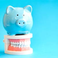 Piggy bank atop model teeth representing cost of dental crown in Bellevue